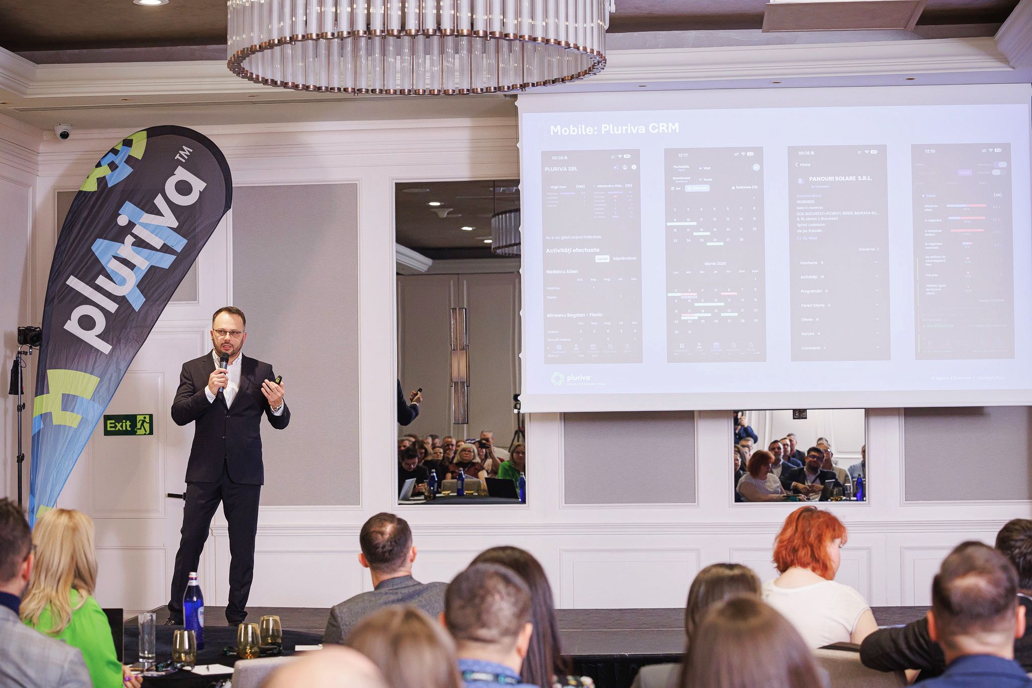 Vorbitor pe scenă, lângă slide-ul cu aplicația mobilă Pluriva CRM