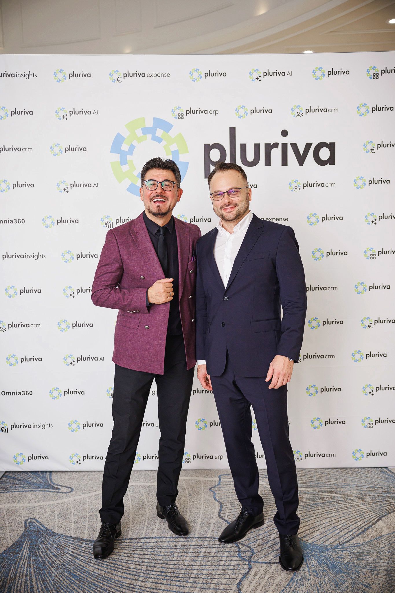 Două persoane pozând în fața panoului cu logouri Pluriva